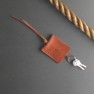 A set of keys lay on a table attached to a square, brown leather pouch.